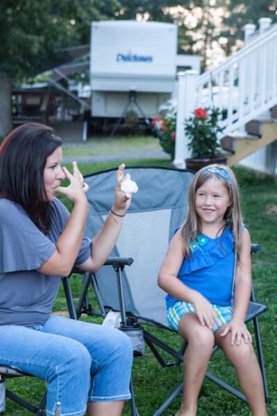 Lady licking fingers with marshmallow in other hand, little girl smiling at her